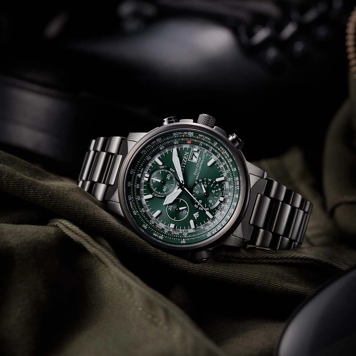 Citizen watch with green face and metal band on green fabric background.