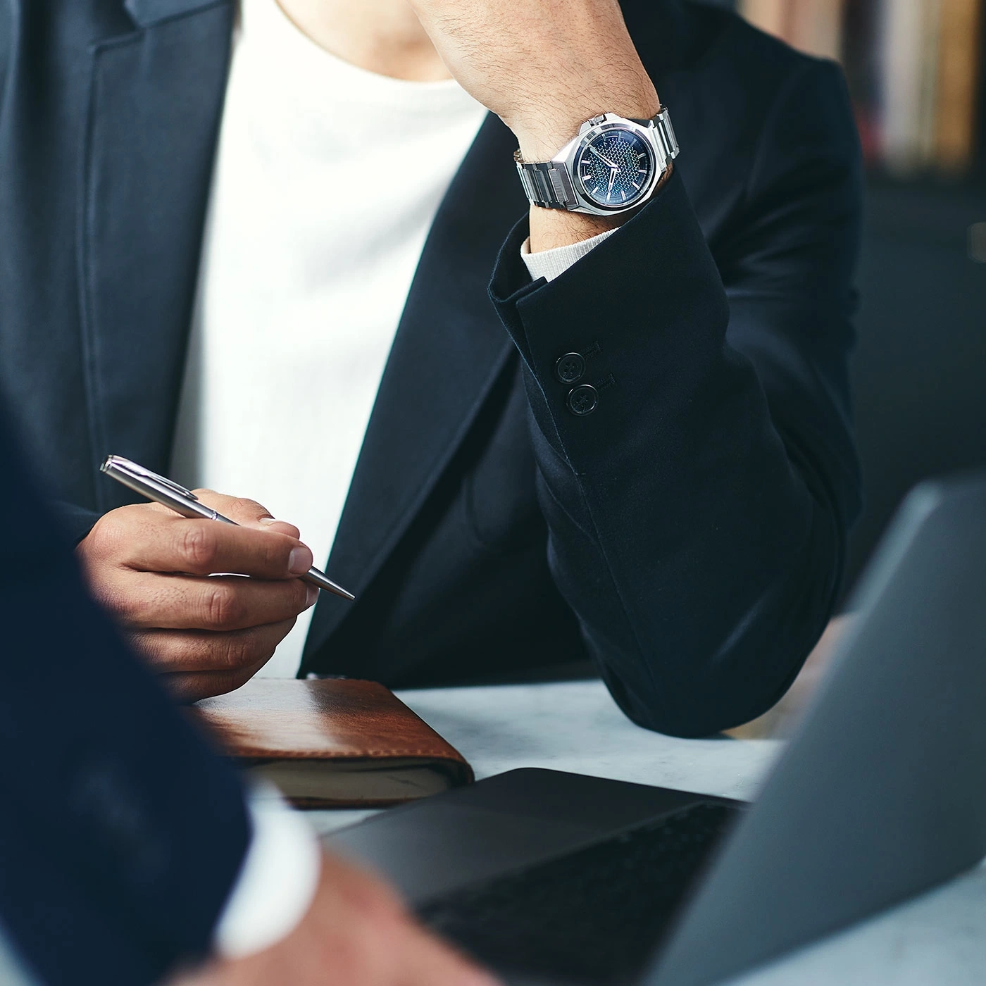 Man in suit with watch and pen, working on laptop, business meeting.