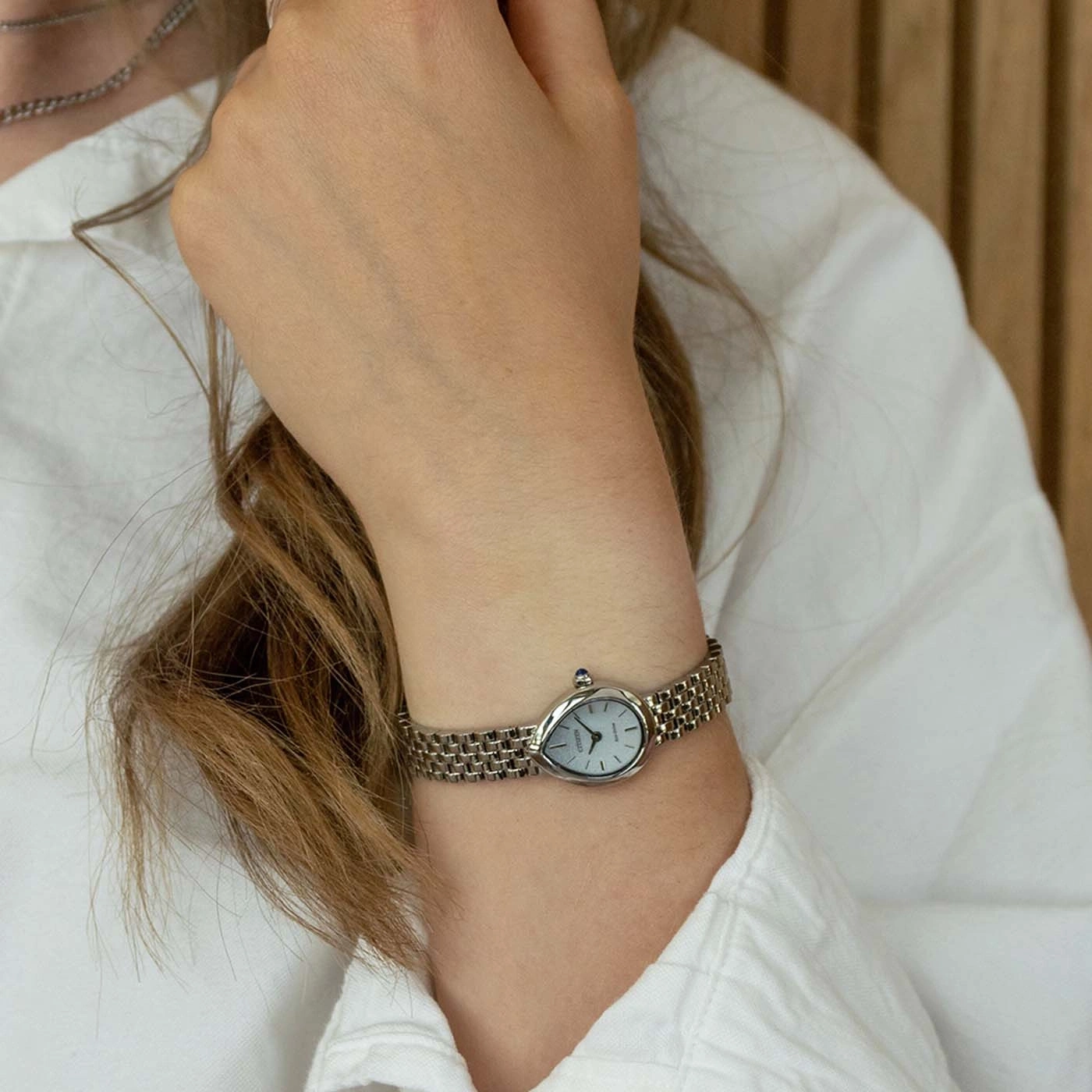 Woman wearing a silver wristwatch with a white face and a blue stone detail.