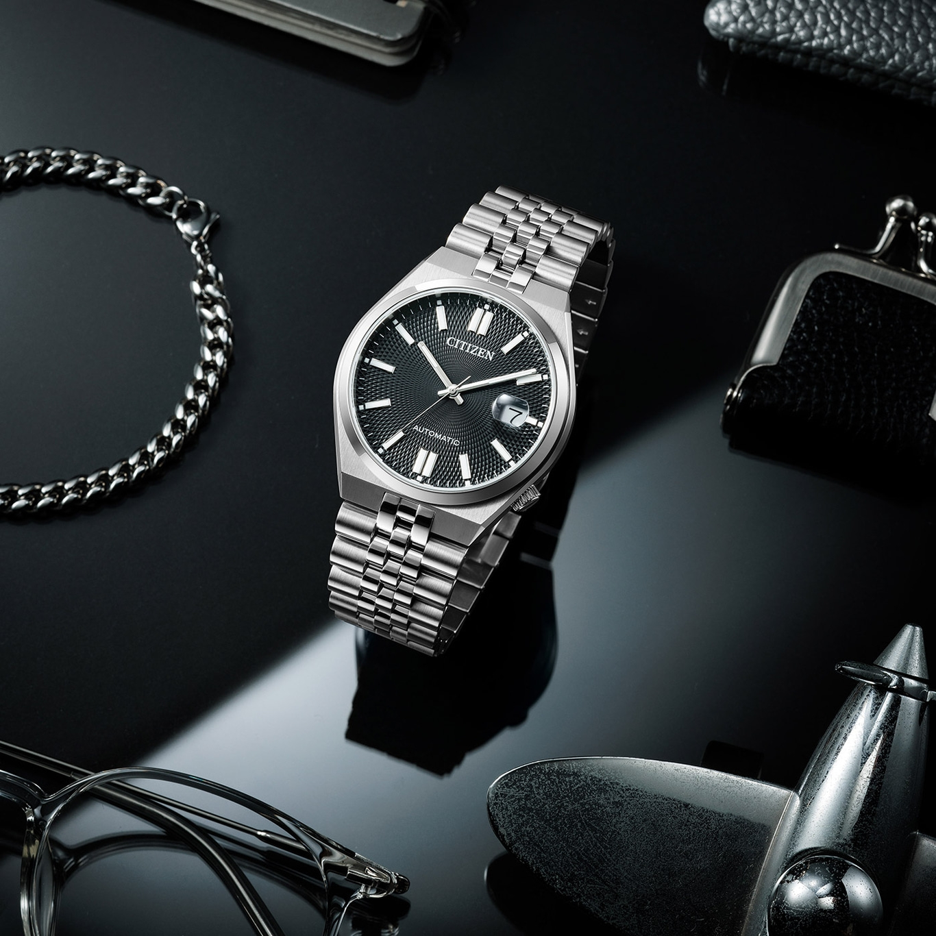 Citizen watch with bracelet, glasses, and accessories on a black surface.