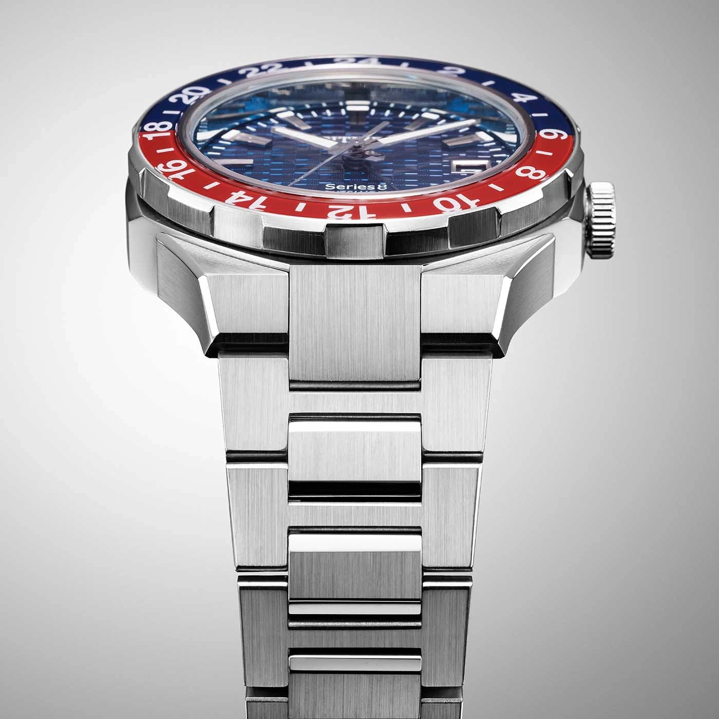 Close-up of a silver watch with a blue and red bezel and a metal strap.