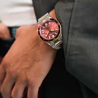 A man wears a red Citizen automatic watch on his wrist, with a grey suit.