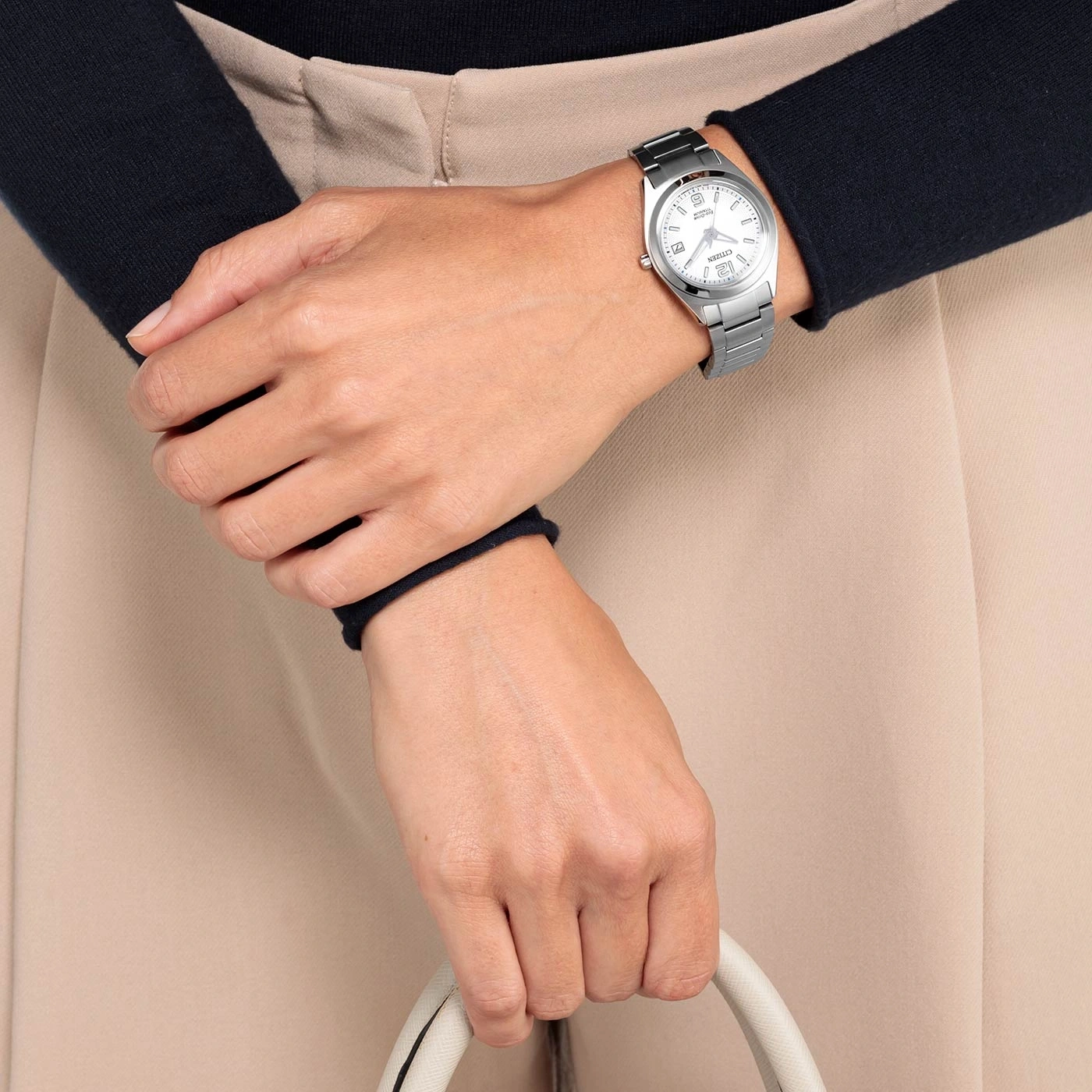 Woman wearing a silver watch, holding a white handbag, beige pants.