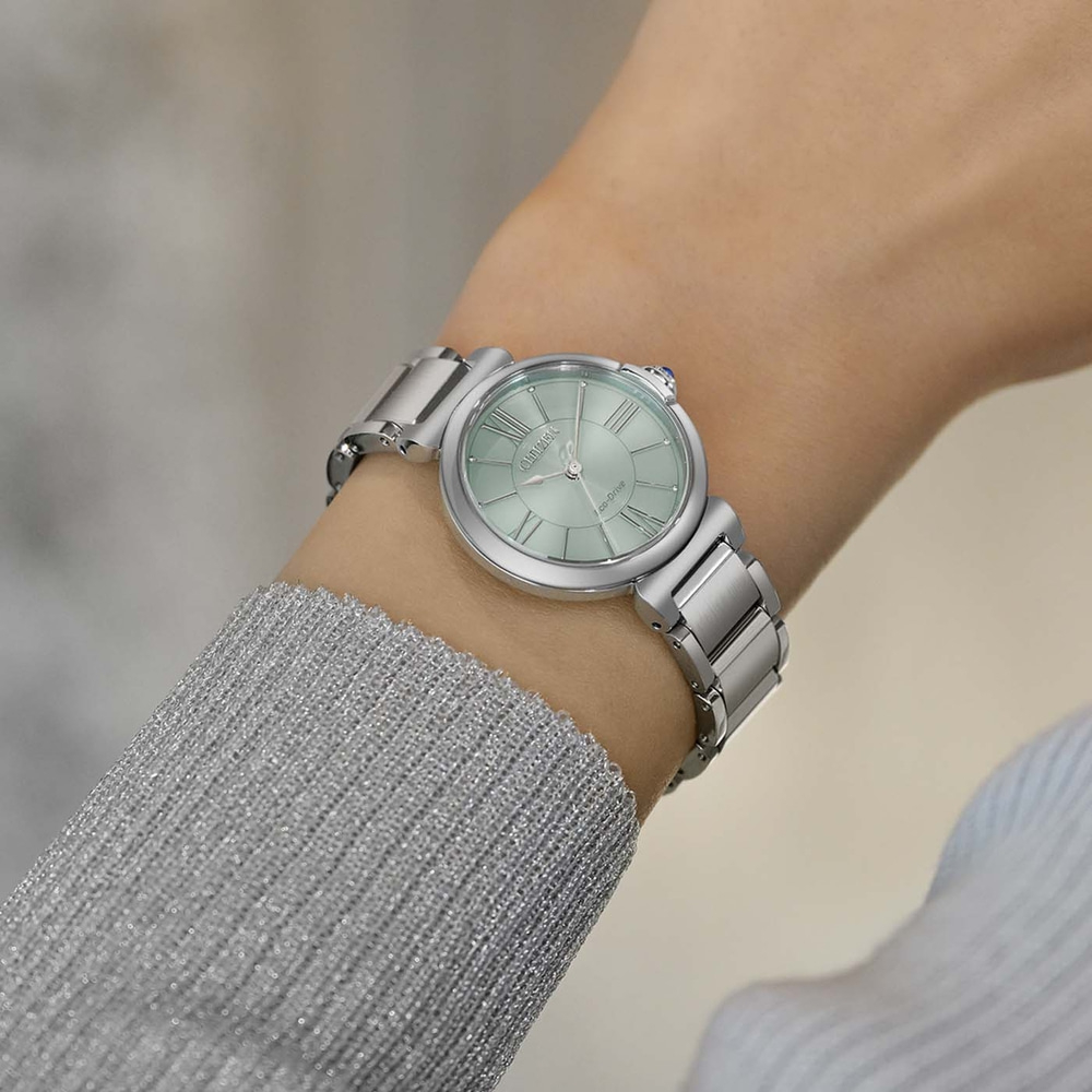 A woman's wrist wearing a silver watch with a light green face.