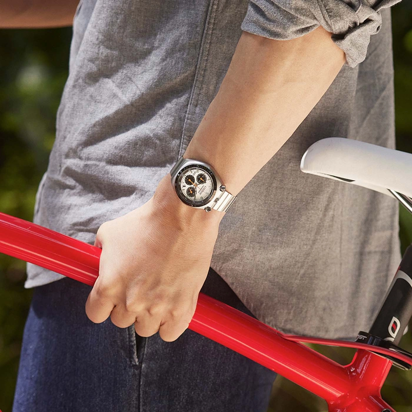 Person in grey shirt holding red bicycle frame, wearing a watch.