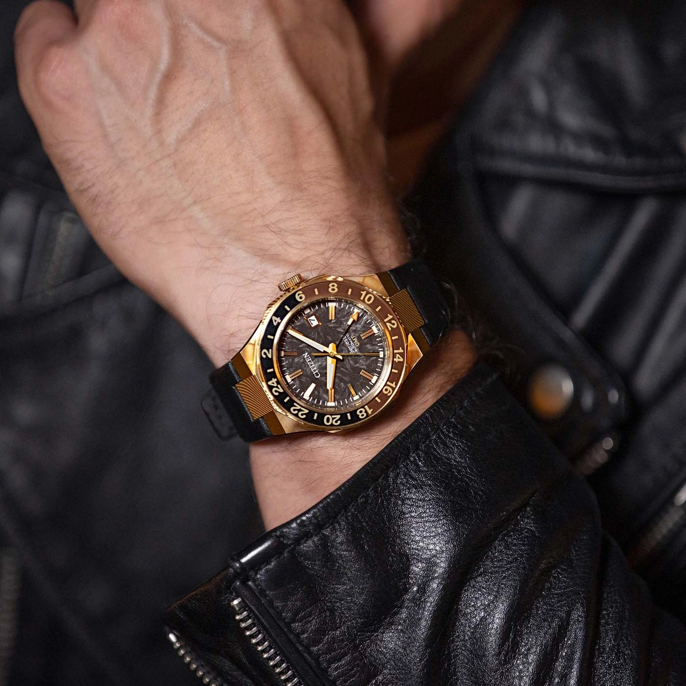 A man wearing a gold and black Citizen watch on his wrist, dressed in a black leather jacket.