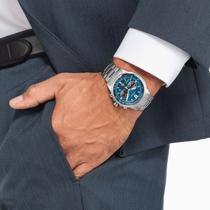 Man wearing a blue watch with a blue suit and white shirt, hand in pocket.