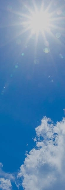 Bright sun in a blue sky with some fluffy white clouds.