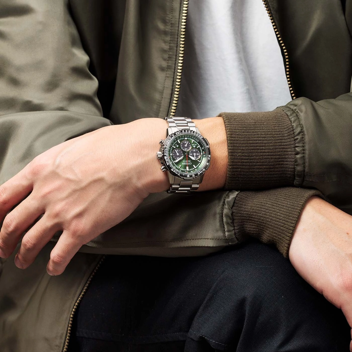 Man wearing a silver watch with a green face and a green jacket.