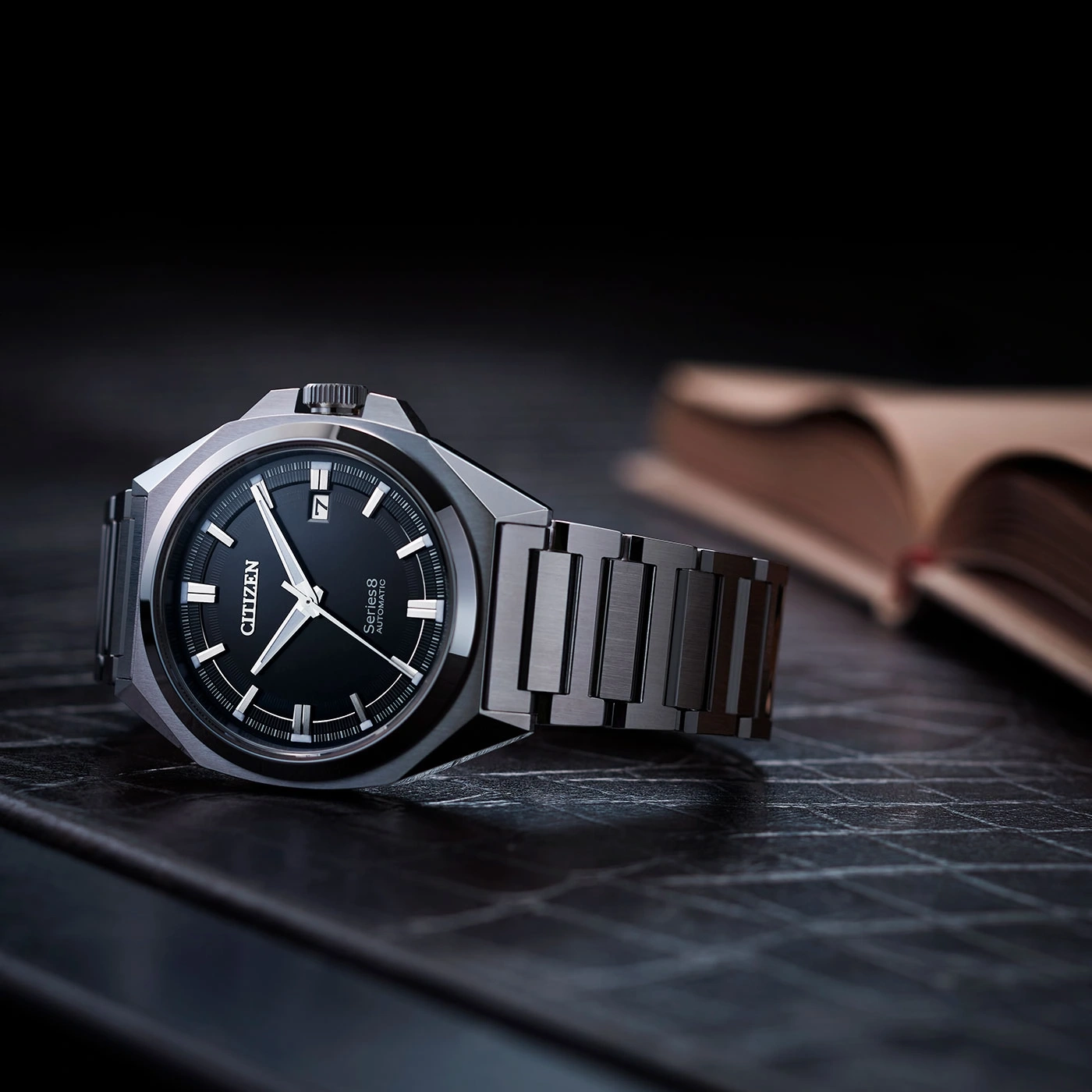 Citizen watch with black face and metal band on a dark surface.