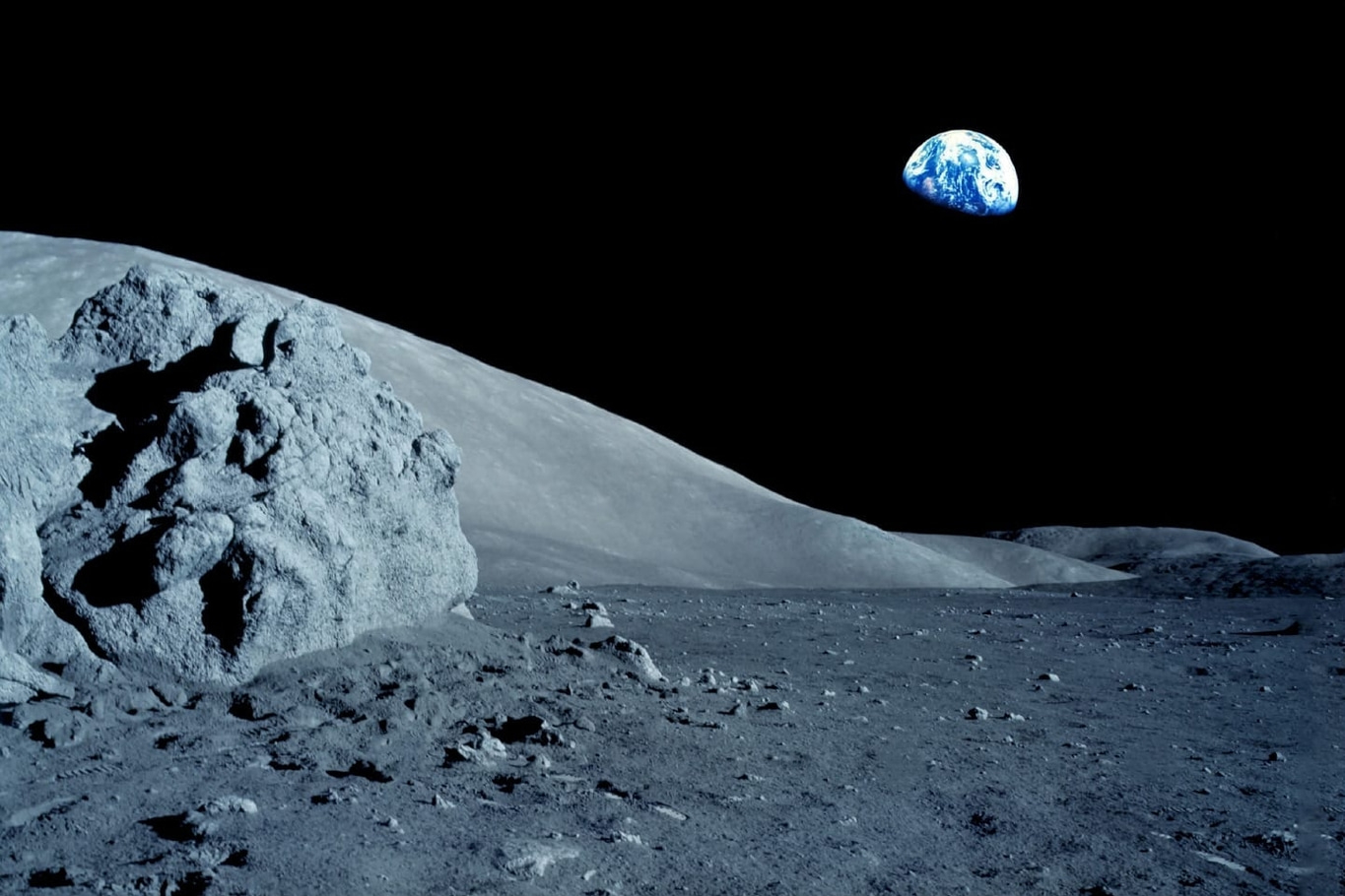 Moon surface with Earth in the sky, a rocky landscape and a dark background.