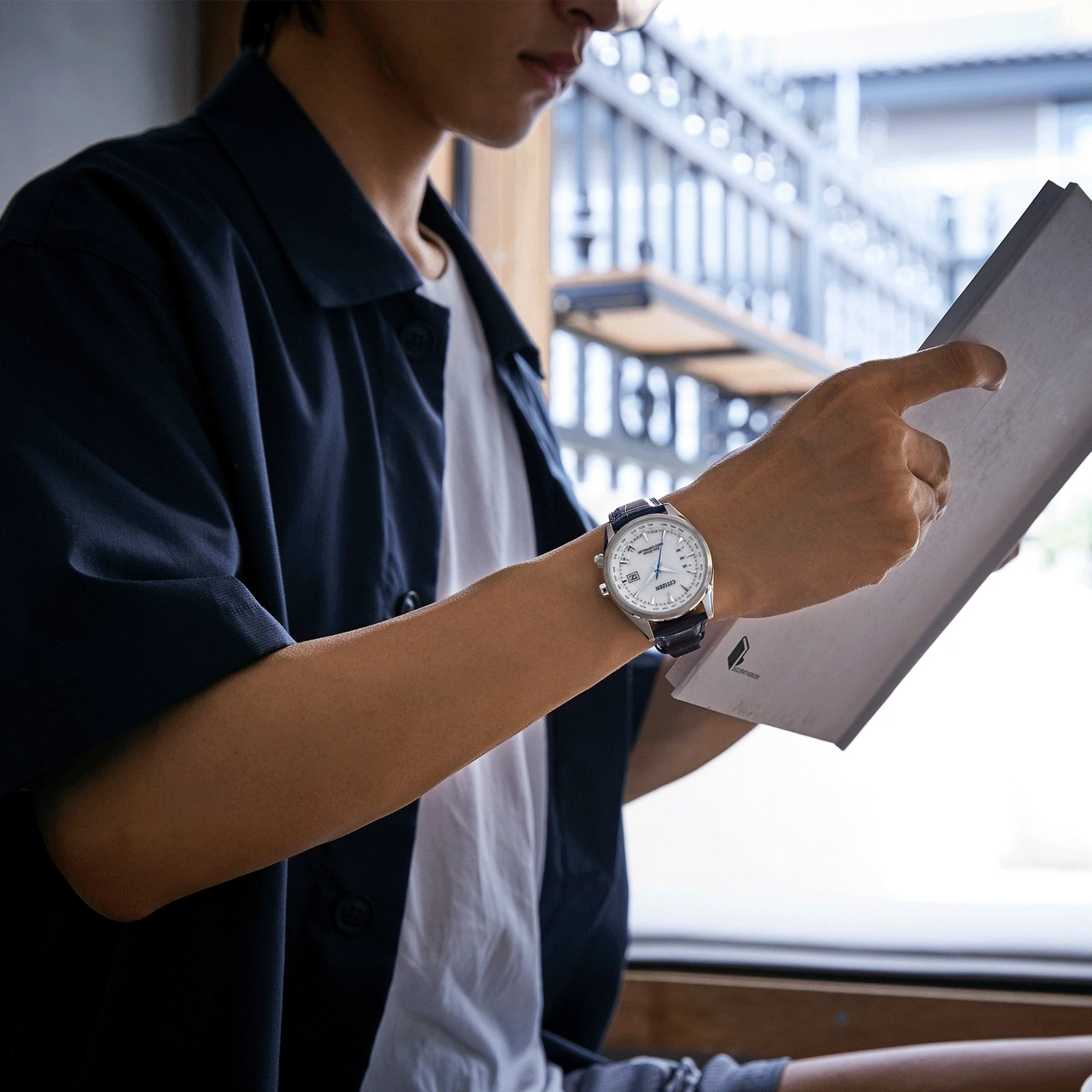 Man wearing a watch, reading a paper, with a blue jacket and white shirt.