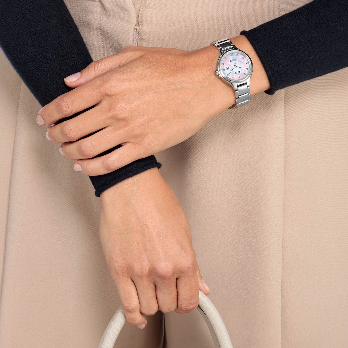 Woman wearing a watch, holding a bag, with a black sleeve and beige pants.