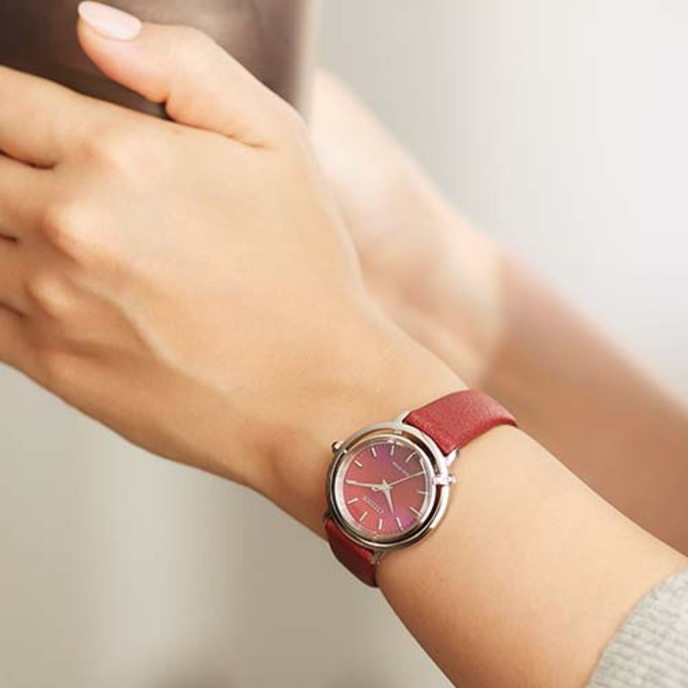 A woman's wrist with a red watch. The watch has a red strap and a silver case.