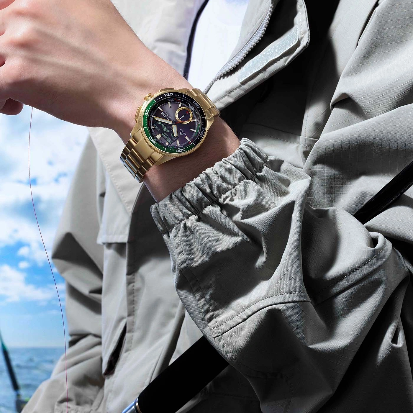 Gold watch on a man's wrist, fishing rod in background.
