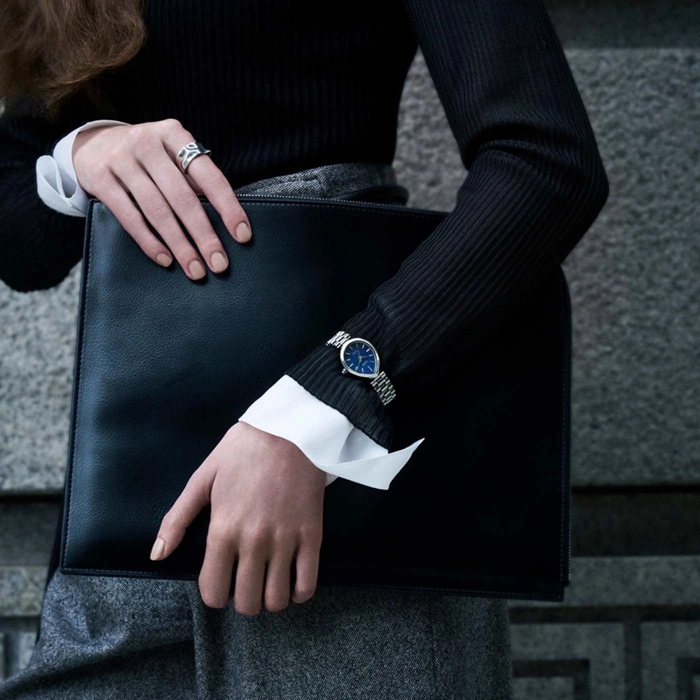 Woman holding black briefcase, wearing watch and ring.
