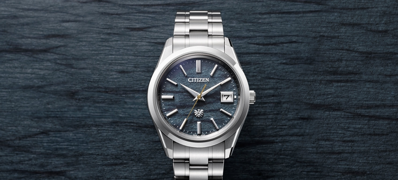 Citizen-Uhr mit blauem Zifferblatt und silbernem Armband auf dunklem Hintergrund.
