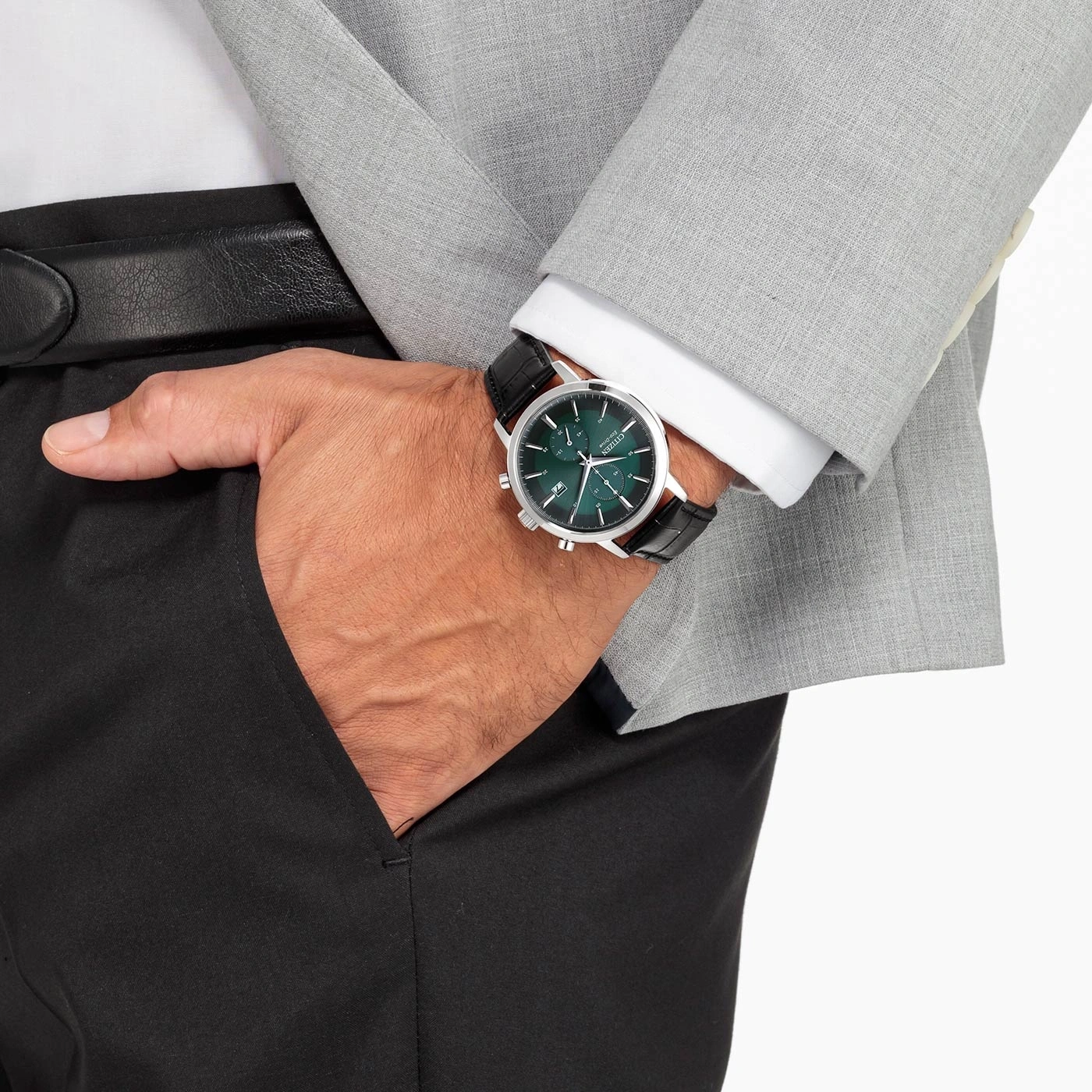 Man wearing a watch, suit, and black pants with his hand in his pocket.