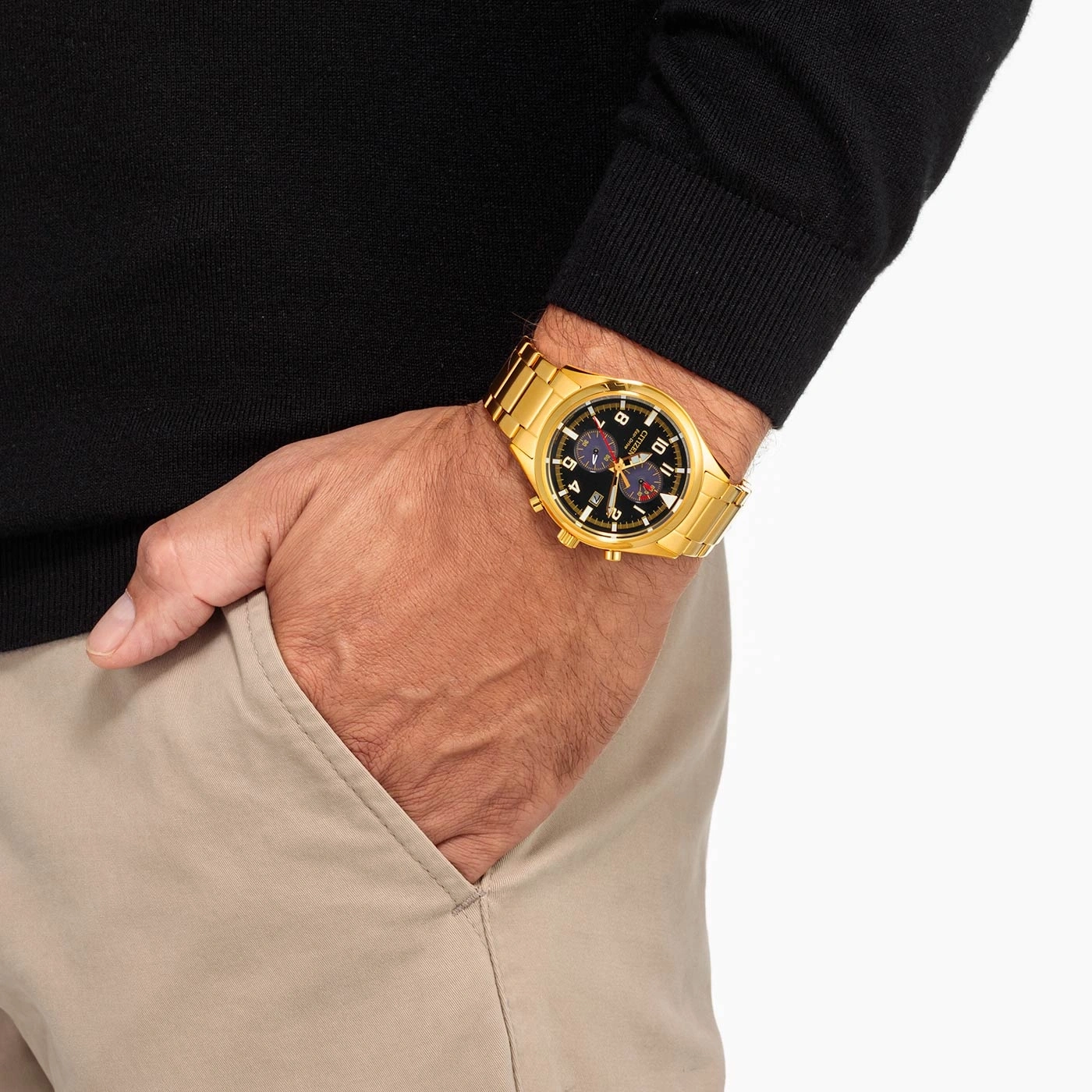Man wearing a gold watch, black sweater, and tan pants.