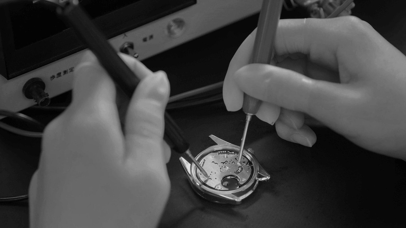 Hands working on a watch with tools, close-up shot, black and white.