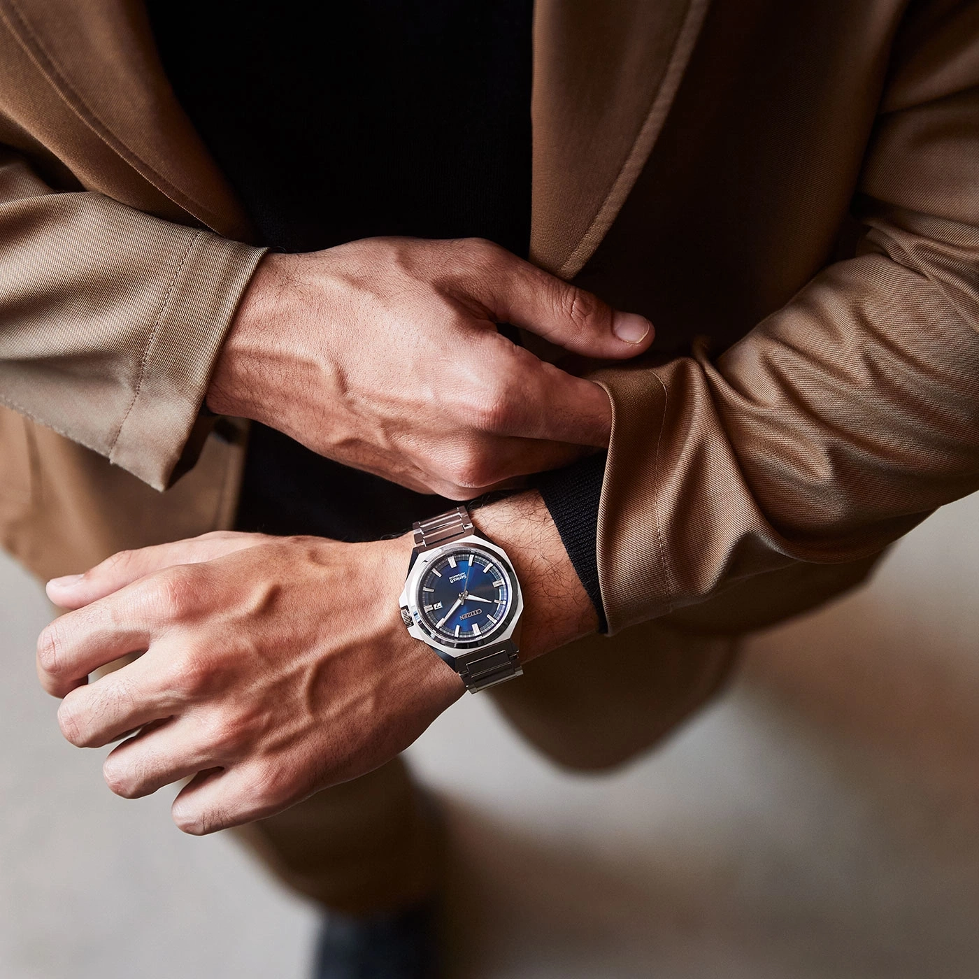 Man wearing a watch, suit jacket, and black shirt, close-up shot.