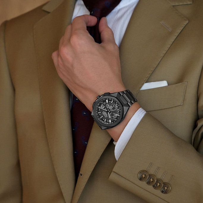 Man in suit adjusting tie, wearing a black watch, close-up shot.