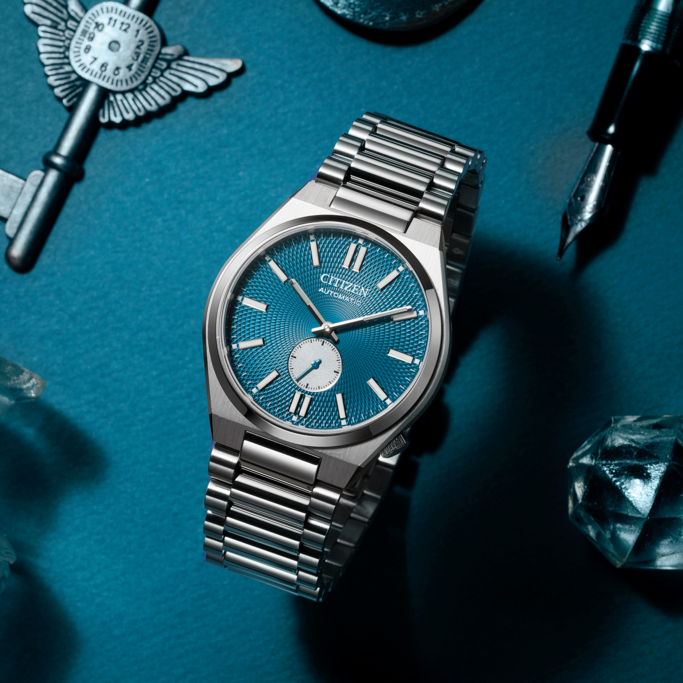 Citizen watch with blue face, key, pen, and crystals on blue surface.