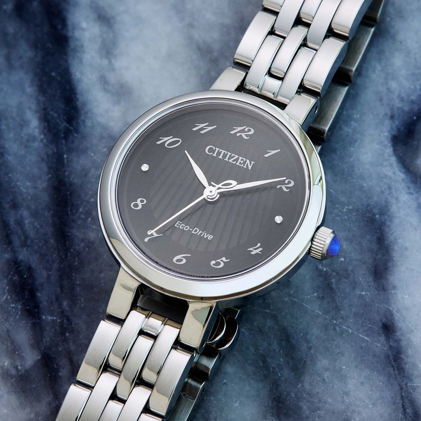 Citizen watch with a dark face and silver band on a marble surface.