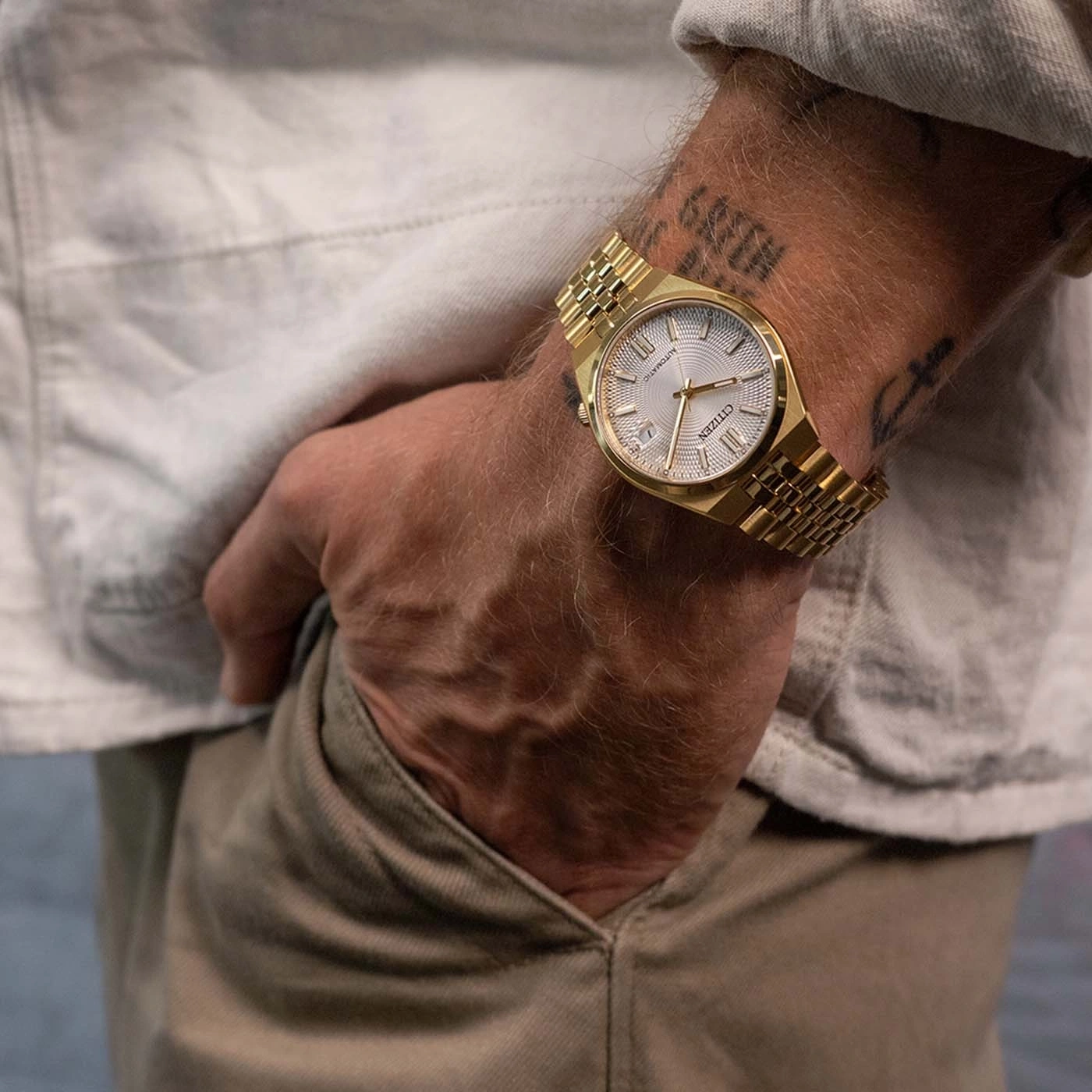 Gold watch on man's wrist with tattoos.