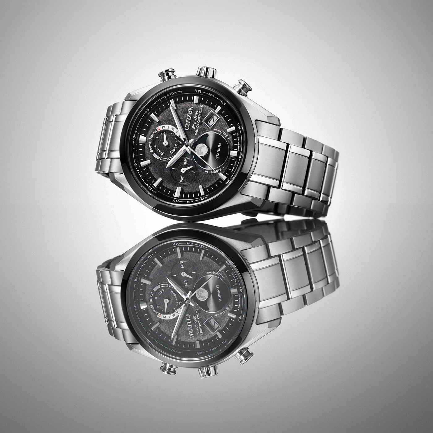 Citizen watch with a black face and silver band, reflected on a surface.