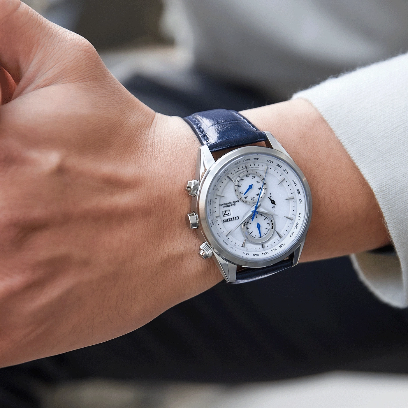 Close-up of a Citizen watch on a wrist, blue leather strap, white dial, silver case.