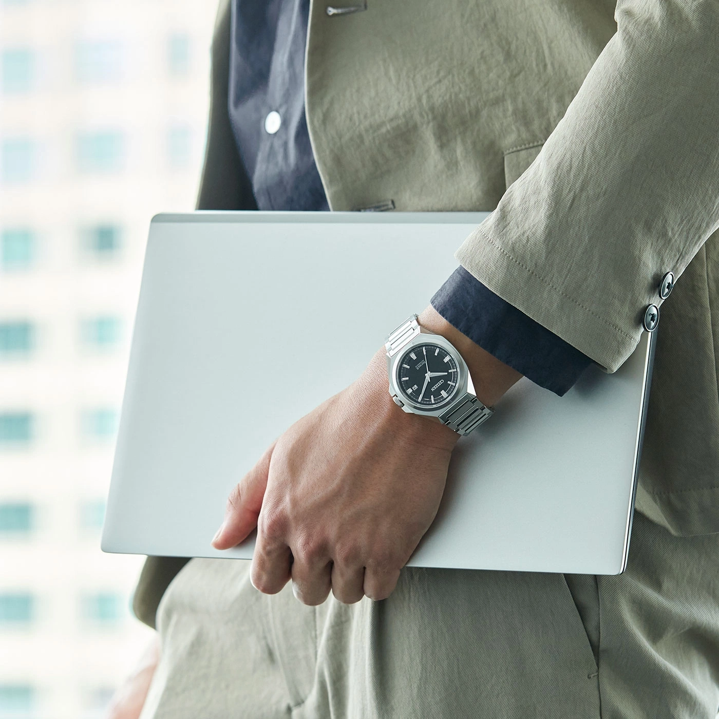 Man holding laptop, wearing watch and suit. Business professional.