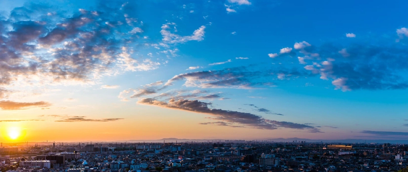Cityscape at sunset with a vibrant sky and scattered clouds over buildings.