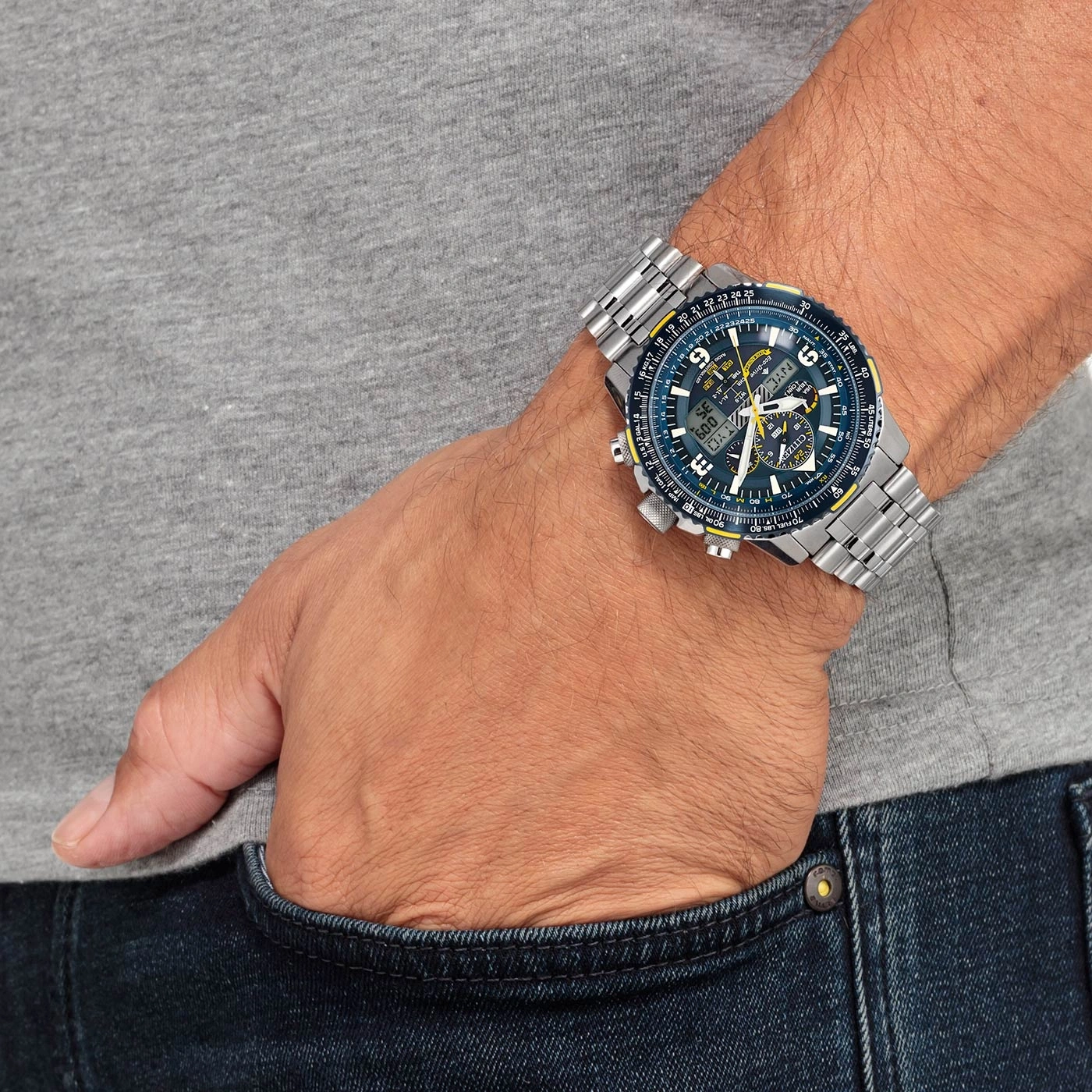 Man wearing a Citizen watch, hand in pocket, gray shirt, blue jeans.
