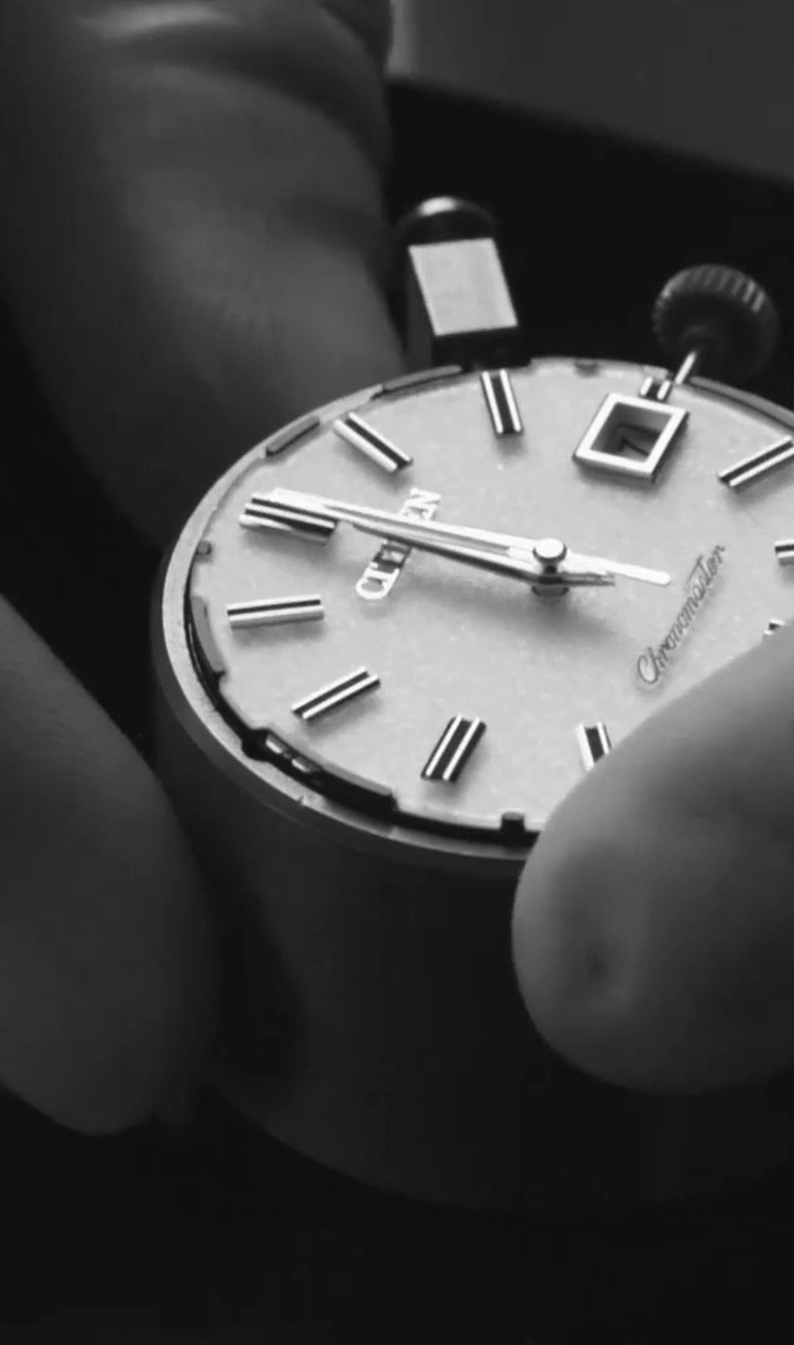 Close-up of a watch face with hands and markers, held by fingers.