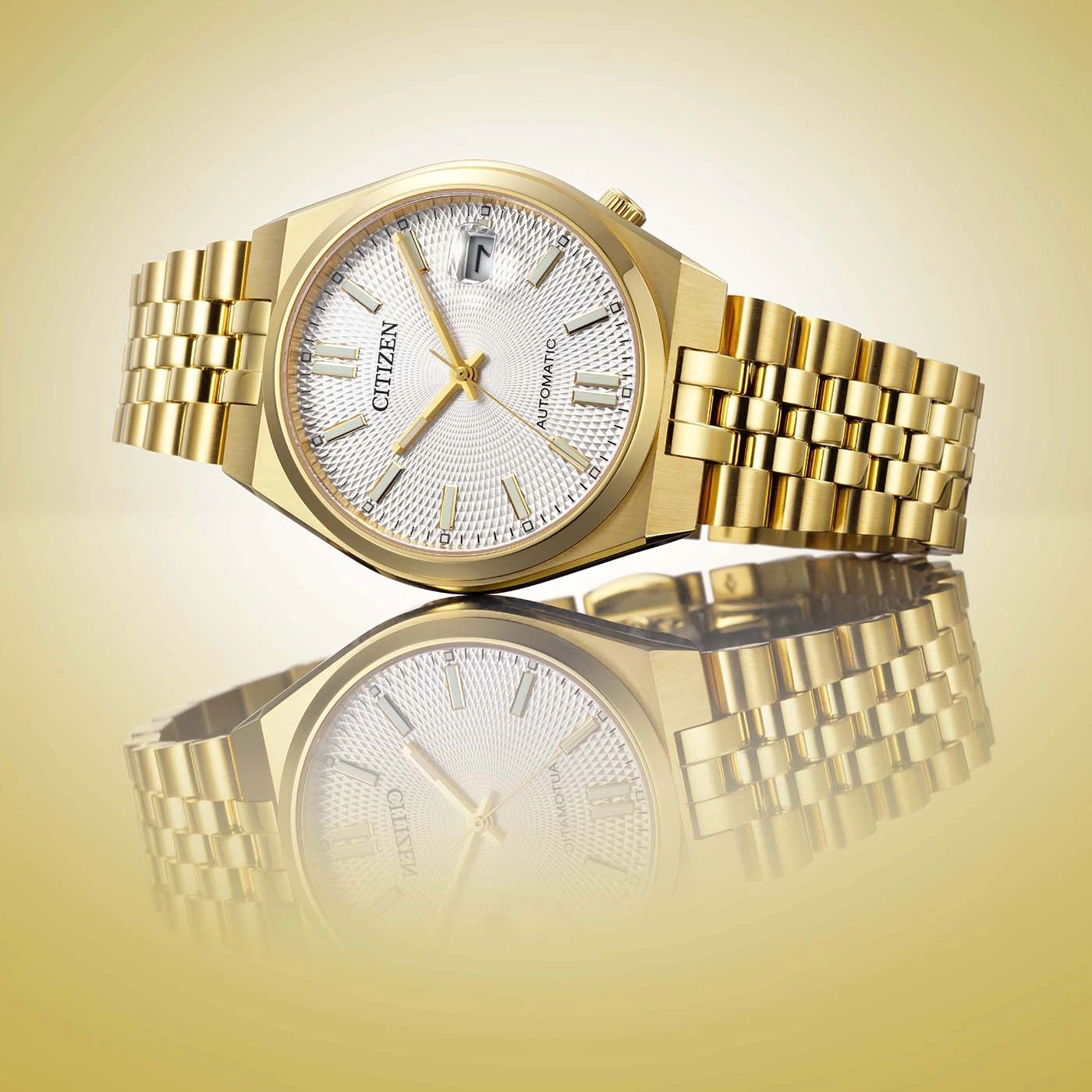 A close-up studio shot of a luxurious gold Citizen automatic watch with a white patterned dial and a matching bracelet, reflected on a golden surface.