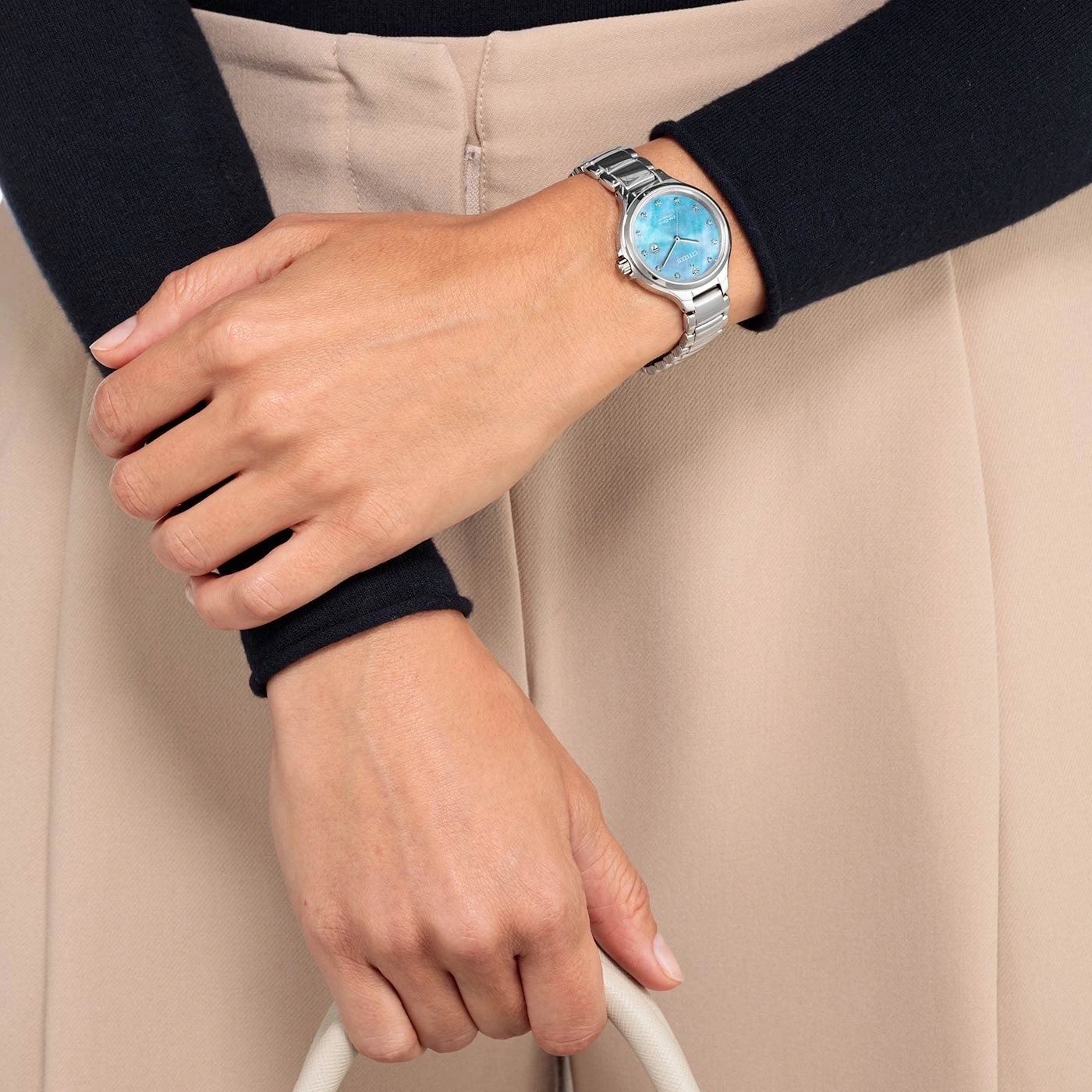 Woman wearing a silver watch with a blue face, holding a white bag.