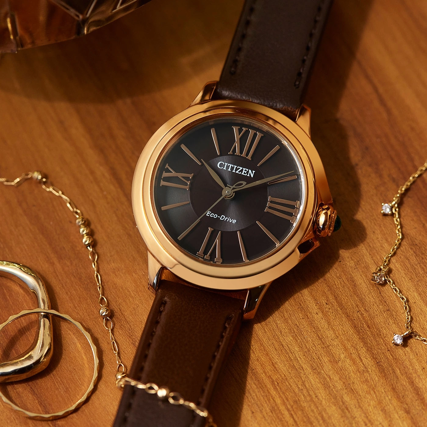 Citizen watch with brown leather strap and gold accents on wooden surface with jewelry.