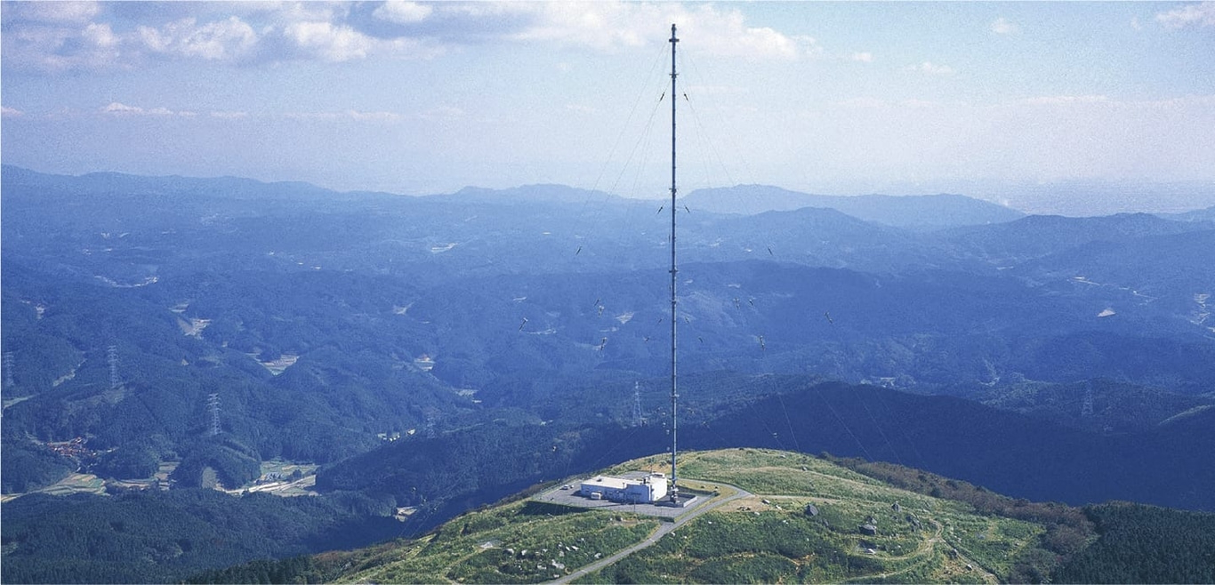 A tall radio tower on a mountain with a beautiful landscape.