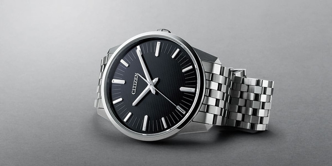 Citizen-Uhr mit schwarzem Zifferblatt und silbernem Armband auf grauem Untergrund.