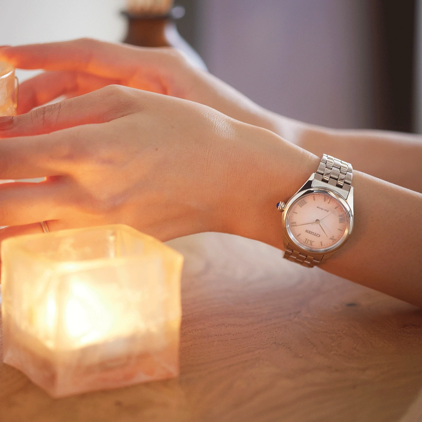 Woman's wrist with a watch, lit candle, and wooden table.