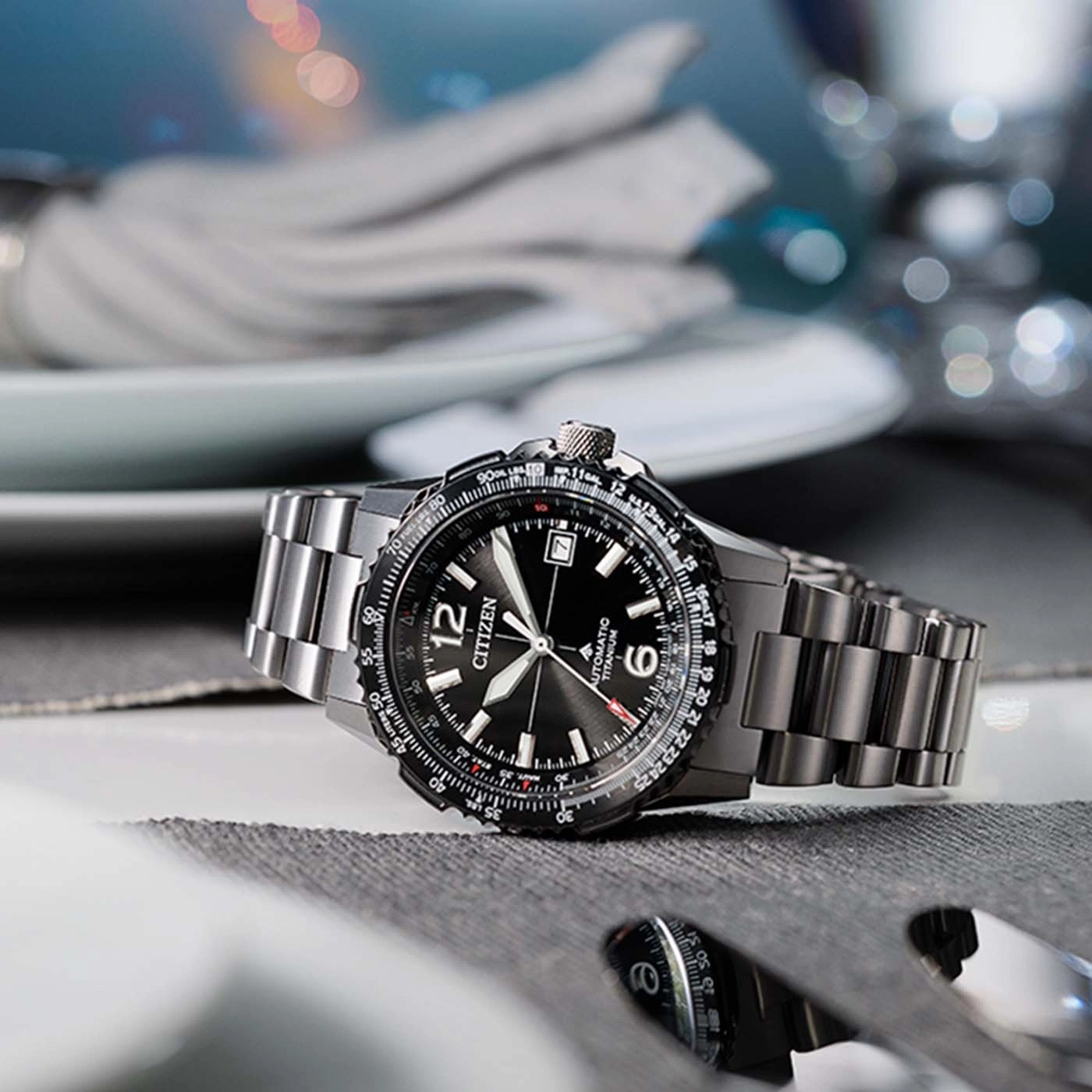 A black Citizen automatic titanium watch on a table with cutlery.