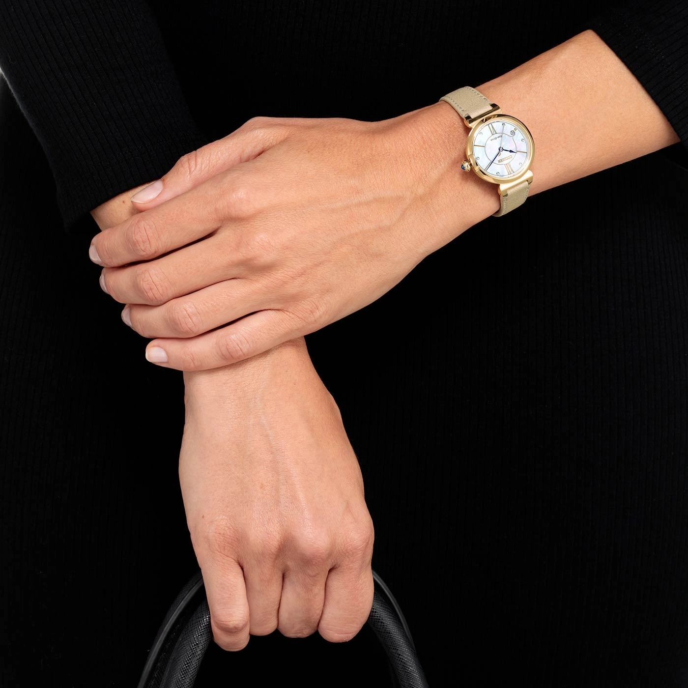 Woman wearing a gold watch, holding a black bag, black dress