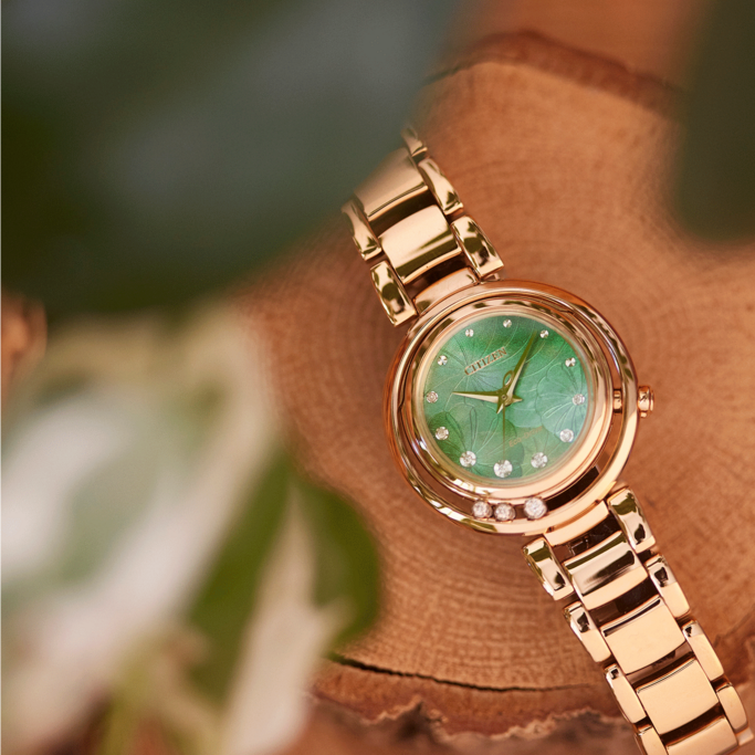 Gold Citizen watch with green face and diamonds on wooden surface.
