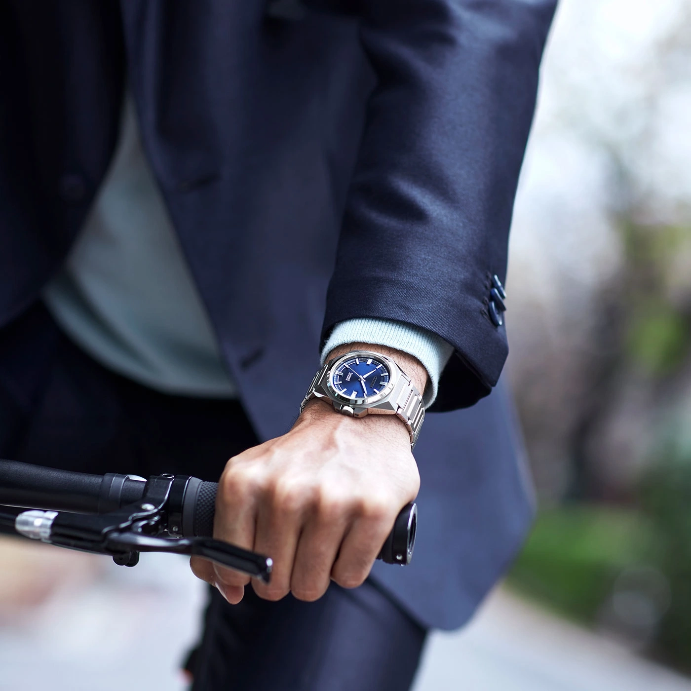 Man wearing a watch, holding a bicycle handlebar, wearing a suit.
