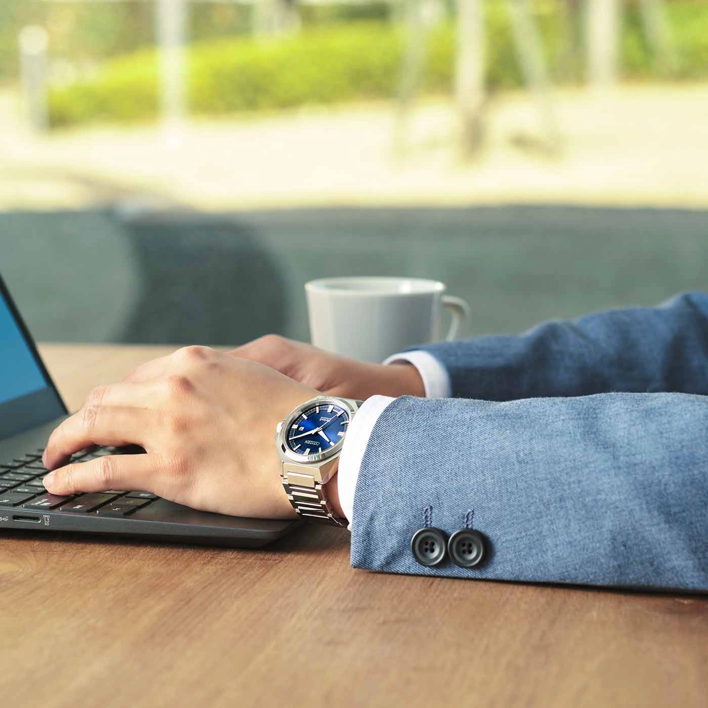 Man wearing a watch, typing on a laptop, with a cup of coffee.