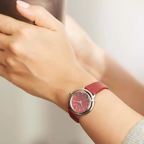 A woman's wrist with a red watch. The watch has a red strap and a silver case.