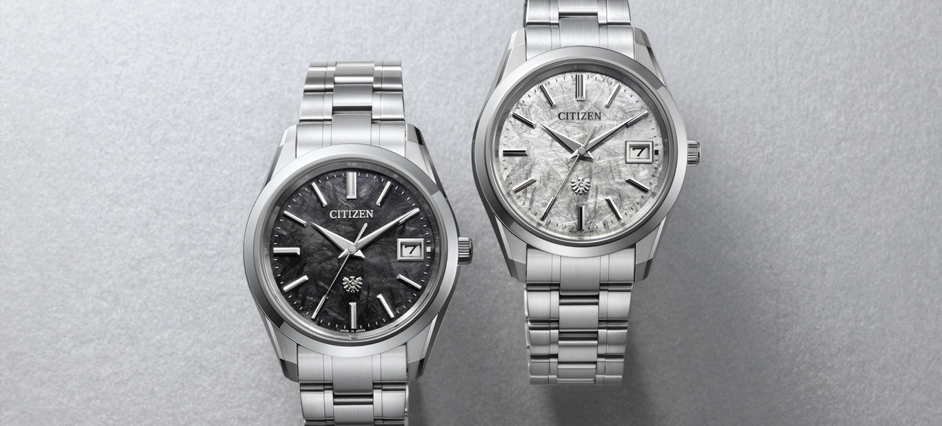 Zwei Citizen-Uhren mit strukturierten Zifferblättern und Metallarmbändern auf grauem Hintergrund.