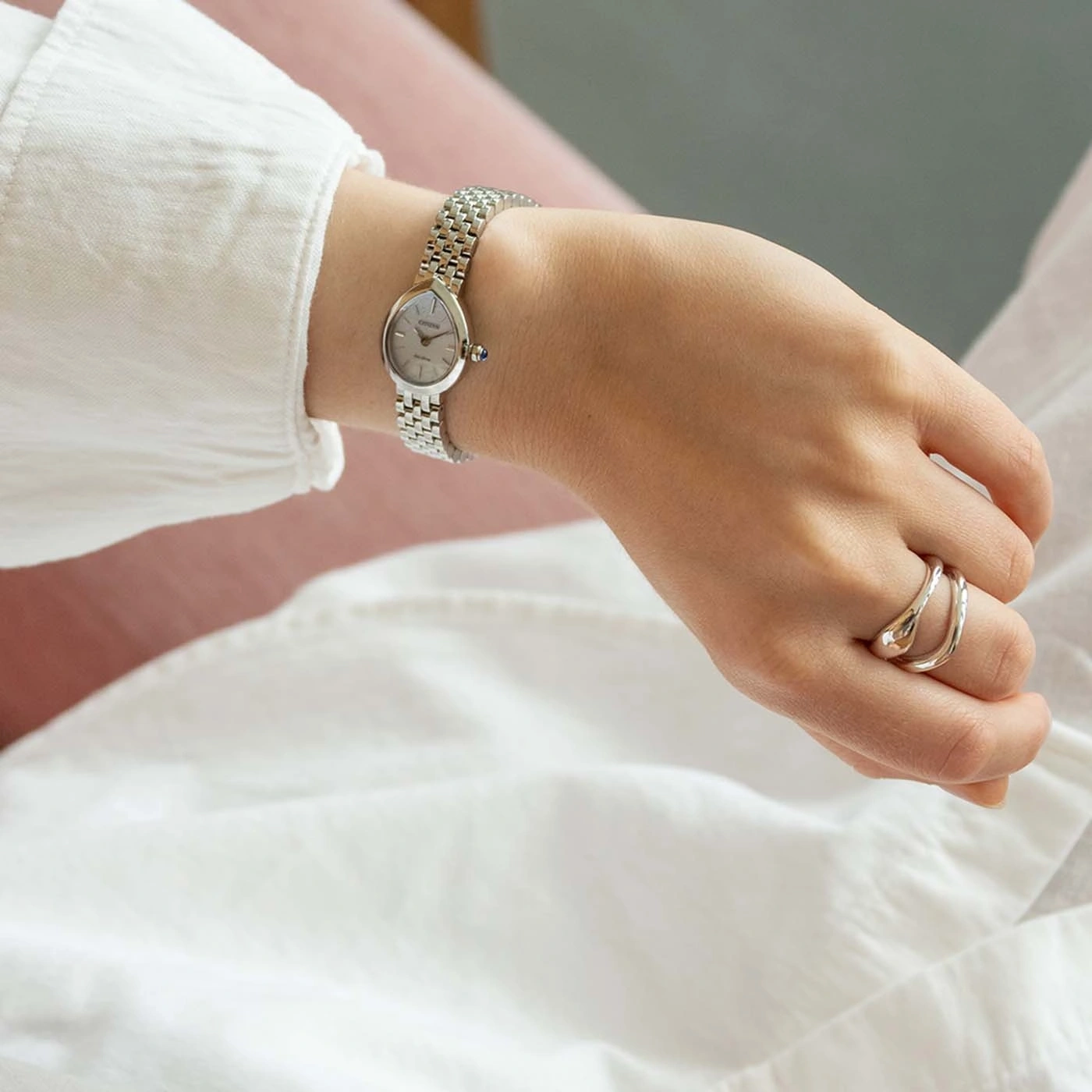 A woman's hand wearing a silver watch and rings.