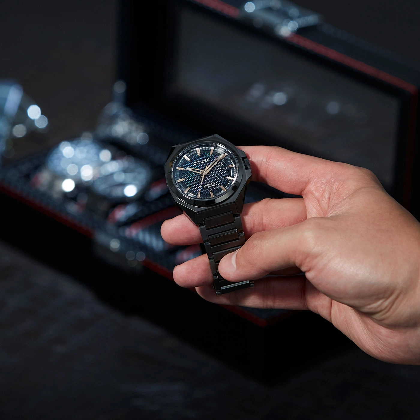 A person holding a black Citizen watch with a dark background.